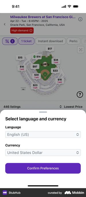 StubHub sheet headed Select language and currency over a stadium seat map. Two dropdowns are shown, Language set to English US and Currency set to United States Dollar, above a purple button reading Confirm Preferences
